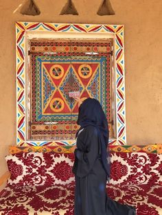 a woman wearing a blue veil standing in front of a colorful wall hanging on the side of a building