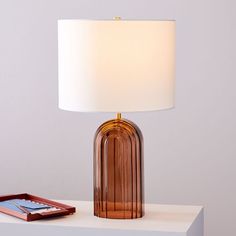 a table lamp sitting on top of a white shelf next to a cell phone and remote control