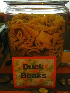 a jar filled with chips sitting on top of a table next to rocks and a sign that reads duck beaks