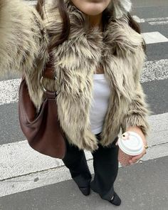 a woman is standing on the street holding a coffee cup and wearing a fur coat