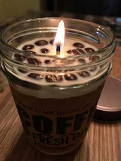 a lit candle sitting on top of a wooden table next to a jar of coffee