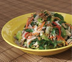 a yellow bowl filled with salad on top of a wooden table