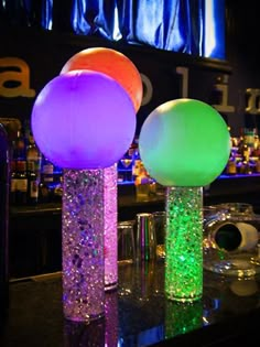 three different colored balloons sitting on top of a counter next to glasses and bottles in front of a bar