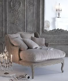 an old fashioned chaise lounge with candles on the floor in front of a mirror