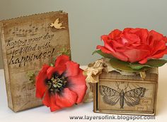 two red flowers are sitting next to a small box with a butterfly on it and an old card