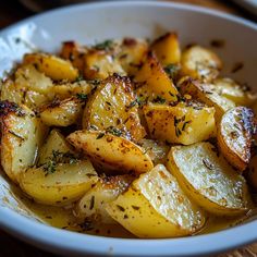 a white bowl filled with potatoes covered in seasoning on top of a wooden table