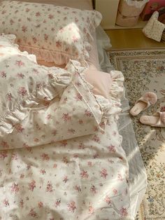 an unmade bed with pink and white floral comforter, pillows and slippers