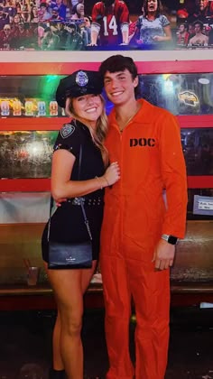 a man and woman in orange jumpsuits posing for a photo with a large poster behind them