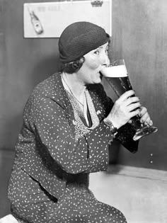 a woman sitting on the floor drinking out of a beer glass with her mouth open