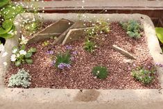 a planter filled with lots of dirt and flowers next to a wooden bench in the background