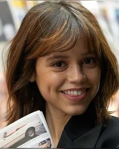 a woman is smiling and holding up a magazine