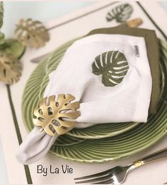 a green and white place setting with napkins, silverware and gold utensils