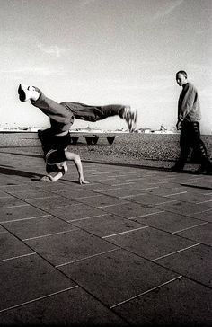 a man doing a handstand on his skateboard in front of another man