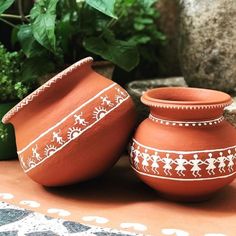 two clay pots sitting on top of a table next to potted plants and rocks