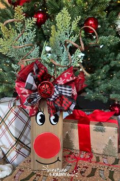 a wooden reindeer head sitting in front of a christmas tree with red and black bows