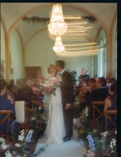 a bride and groom kissing in front of an audience at a wedding ceremony with chandeliers hanging from the ceiling