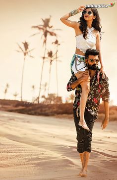 a man carrying a woman on his back while walking down the beach with palm trees in the background