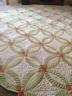 a large green and white quilt on the floor in front of a television set with an orange border