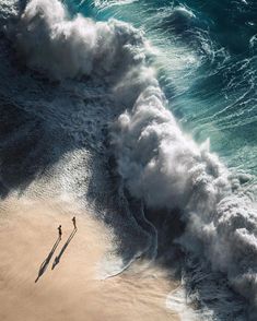 an aerial view of the ocean with waves crashing over it and a lone person standing in the sand