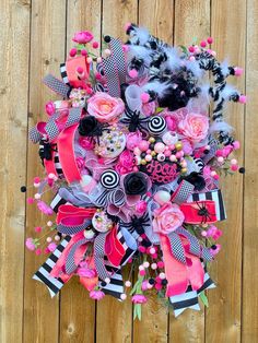 a pink and black wreath with feathers, flowers and other decorations on a wooden surface