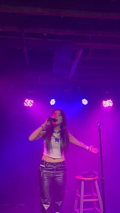 a woman standing in front of a microphone on top of a purple light filled stage