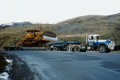 two large trucks are parked on the side of the road in front of a mountain