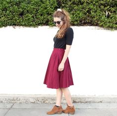 a woman standing on the sidewalk wearing a skirt and black t - shirt with brown shoes