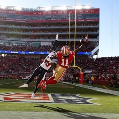 two football players are in the air during a game, one is jumping into the air to catch the ball