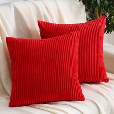 two red pillows sitting on top of a white couch next to a potted plant