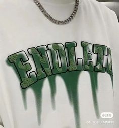 a person wearing a white shirt with green spray paint on it and a chain around their neck