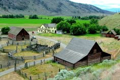 an old western town in the middle of a green field with mountains and fields behind it