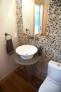 a white sink sitting next to a toilet in a bathroom under a window with rocks on the wall