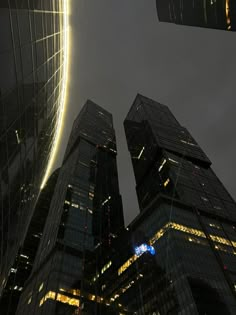 some very tall buildings in the city at night with lights shining on them and one building is lit up