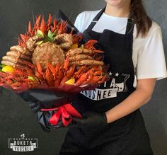 a woman wearing an apron holding a bouquet of lobsters and crab legs in front of a black background