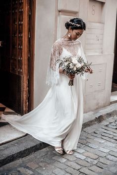 a woman is walking down the street in a white dress and holding a flower bouquet