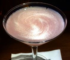 a drink in a glass on top of a wooden table next to a white napkin