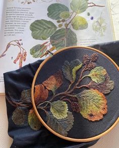 an embroidered leaf and acorn design on a black cloth with a book in the background