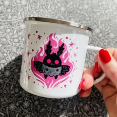 a hand holding a white coffee cup with pink and black designs on the side,