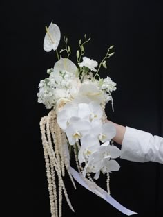 a woman holding a bouquet of flowers with white orchids and pearls on the stems