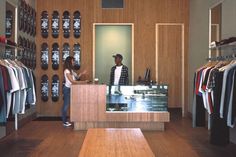 a man and woman standing in front of a clothing store counter with shirts hanging on the wall