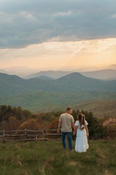 a man and woman standing on top of a lush green hillside under a cloudy sky