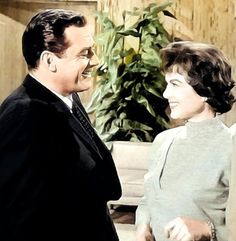 a man and woman standing next to each other in front of a potted plant