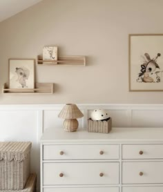 a baby's room with white dressers and pictures on the wall above them