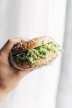 a hand holding a sandwich with lettuce and sesame seeds on it, in front of a white background