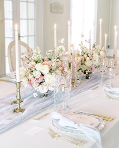 the table is set with white and pink flowers, gold place settings, and candles