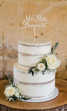 a wedding cake with white flowers and a mr and mrs sign on top is sitting on a tree stump