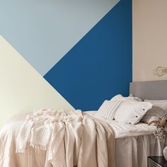 a bed with pillows and blankets on it in front of a wall painted blue and white