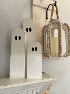 three wooden ghost decorations hanging on a wall next to a white shelf with a candle in it