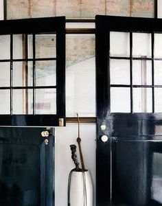 two black doors and a white vase in front of them on the wall next to each other