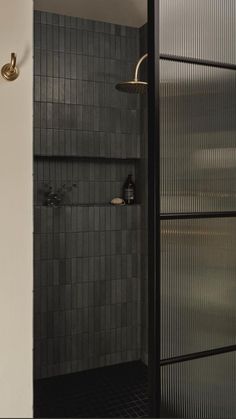 a bathroom with a shower head and black tiled walls, along with an open door